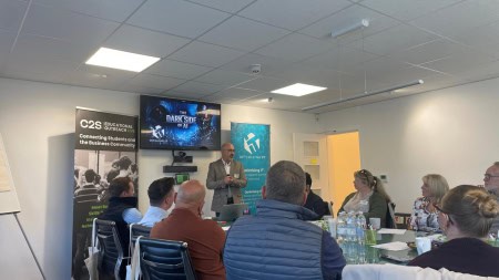 A group of attendees seated around a table, listening to a speaker talk about The Dark Side of AI